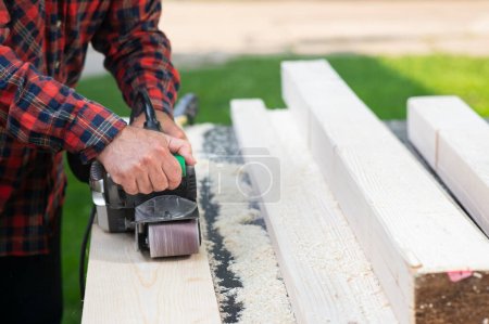 Téléchargez les photos : Hommes travaillant avec la ceinture de ponçage sur panneau en bois à l'extérieur - en image libre de droit