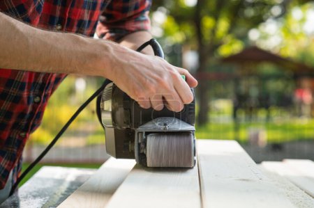 Téléchargez les photos : Le menuisier travaille avec la polisseuse électrique sur le bois - en image libre de droit