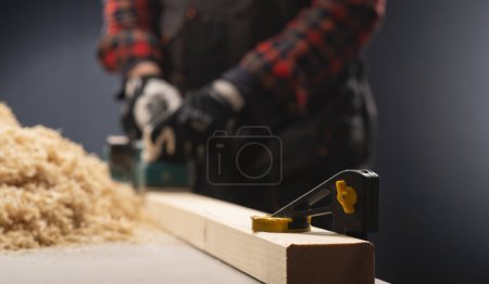 Foto de Herramienta de compresión de abrazadera. Carpintero trabaja con cepilladora eléctrica en taller. - Imagen libre de derechos