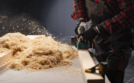 Photo for Carpenter works with electrical planer in workshop - Royalty Free Image