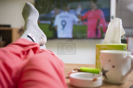 Photo for Watching a football game. Feet up in front of TV. Relaxed home atmosphere. - Royalty Free Image