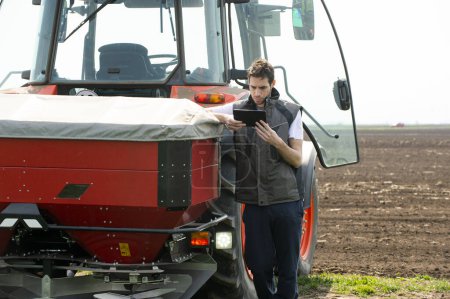 Junge Landarbeiter neben Traktor mit digitalem Tablet.Transport, Landwirtschaft.