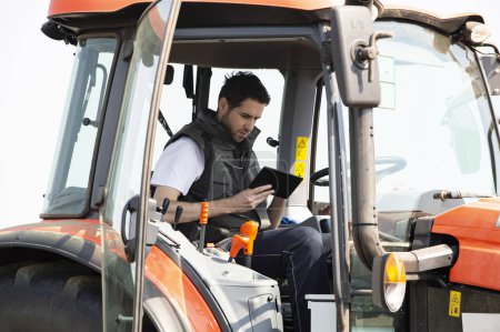 Junge Landarbeiter auf dem Traktor mit digitalem Tablet. Verkehr, Landwirtschaft.