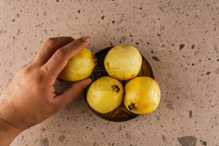 Téléchargez les photos : Fruits de saison d'hiver au Mexique, goyaves géantes sur une assiette en bois sur un fond de carrière rose et une main prenant un fruit. - en image libre de droit