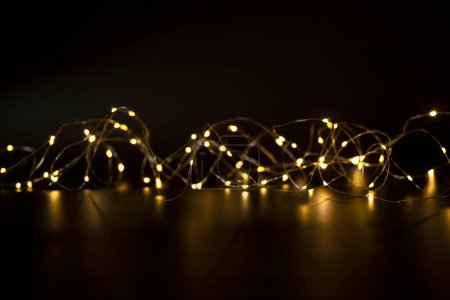 Photo for Glowing New Year's garland with blurry golden bokeh lights. Black background. Concept of Christmas, evening, wishes, illumination. Copy space. Nobody. - Royalty Free Image
