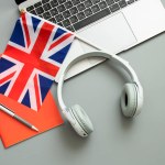 Concept of online learning English, foreign languages, distance education, knowledge, modern technologies for study. Laptop, English flag, headphones, notebook. Grey background. Copy space. Nobody.
