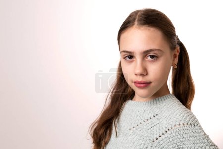 Photo for Cute girl with long blond hair, ponytails looking at camera. Studio portrait, white background. Light green knitted sweater. Caucasian child 10 years old. Concept of pre teen, puberty, growing up. - Royalty Free Image