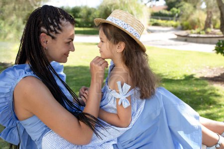 Photo for Daughter and mom in the park. Summer, sunny day. Mother hugs the child's face. Caucasian people, woman with afro braids, girl in stylish straw hat. Outdoor. The concept of family, love, motherhood. - Royalty Free Image