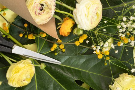 Téléchargez les photos : Préparation pour la fabrication d'un bouquet. Fleurs et ciseaux reposent sur des feuilles vertes. Le concept de floristique, fleuriste, décorations, art. - en image libre de droit