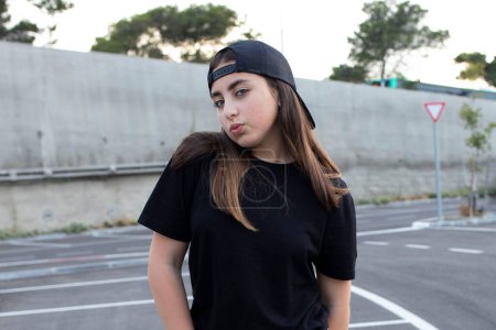Photo for Portrait of a positive, self-confident dancing teenager girl. Outsides. Cool young woman, street style, baseball cap. Sunny day. Natural beauty, lifestyle concept. Caucasian brunette. - Royalty Free Image