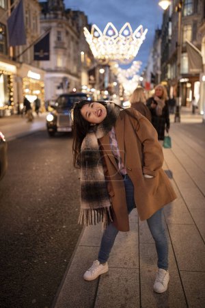 Téléchargez les photos : Belle femme asiatique aux cheveux longs debout sur la rue de la ville européenne du soir décorée de lumières de Noël. Concept vacances d'hiver. - en image libre de droit