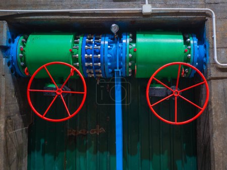 Téléchargez les photos : Tuyau de plomberie avec système de régulation et capteur de pression, deux gros robinet à boisseau sphérique de contrôle manuel rouge de l'eau qui vient au générateur d'énergie sur la centrale hydroélectrique - en image libre de droit