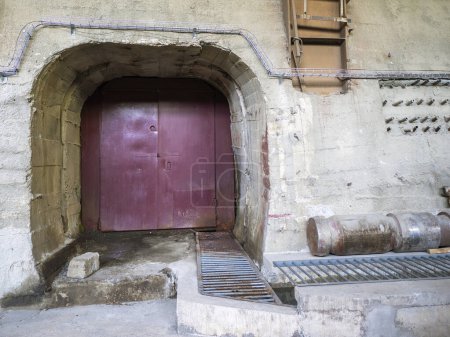 Photo for Old rusty iron dark red colored arch door in concrete wall, industrial interior, entrance to underground passage, concept background - Royalty Free Image