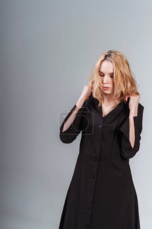 Téléchargez les photos : Portrait d'une fille russe en robe noire sur fond blanc. séance photo de vêtements noirs sur un fond clair. fille blonde en robe de coton noir - en image libre de droit