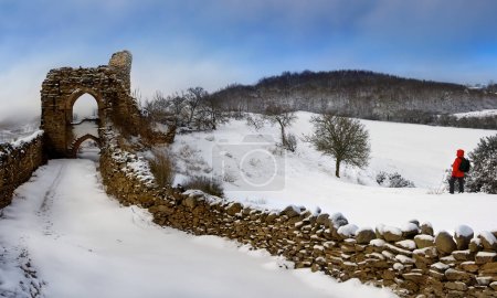 Téléchargez les photos : Un marcheur sur une colline enneigée près des ruines d'un château dans les Highlands d'Écosse. - en image libre de droit