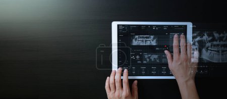 Foto de Manos del dentista que trabajan con la tableta digital para interactuar con VR, x-ray, paciente dientes estudio de educación de tratamiento en línea con AI en fondo oscuro. - Imagen libre de derechos