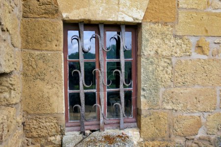 Fenêtre médiévale à meneaux avec grille de sécurité en fer forgé ornée
