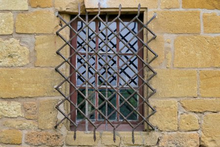 Fenêtre médiévale à meneaux avec grille de sécurité en fer forgé ornée
