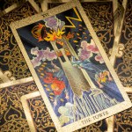 Gold embossed tarot cards on the table. The Major Arcana card The Tower lies facing the viewer. High quality photo