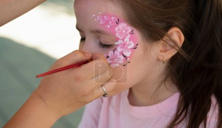 El artista hace un dibujo en la cara de la niña con una pintura de la cara. Foto de alta calidad