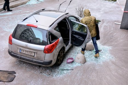 Téléchargez les photos : A man examines a damaged car near an apartment building in Kyiv, which suffered from a kamikaze drone attack by the Russian Federation on the night of December 30, 2022. - en image libre de droit