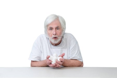 Photo for Horizontal shot of an old man sitting at a table with his hands full of eggs looking very surprised or frightened.  Isolated on white.  Lots of copy space. - Royalty Free Image