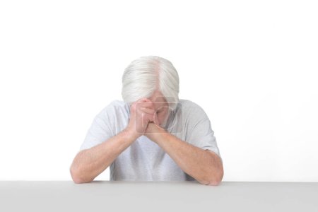 Foto de Horizontal shot of an old man with his elbows leaning on a table head bowed in prayer.  Isolated on white.  Lots of copy space. - Imagen libre de derechos
