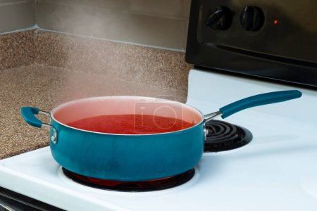 Foto de Horizontal shot of a blue pot on a stove top holding steaming tomato soup. - Imagen libre de derechos