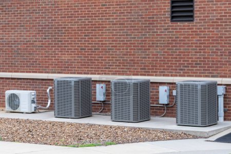 Horizontal shot of four air conditioning compressors outside a school building.