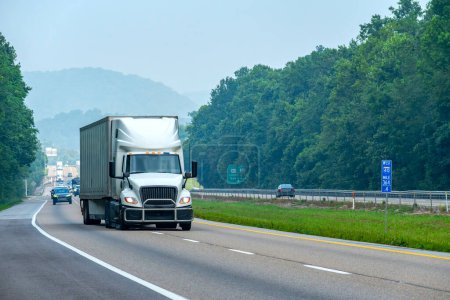 Fotografía horizontal de un camión de caja blanca cambiando de carril en una carretera interestatal.