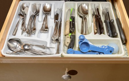 Horizontal shot of the cluttered silverware drawer in some elderly peoples home.