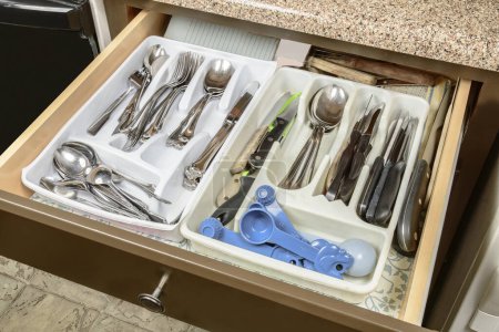 Horizontal shot of a messy and cluttered silverware drawer in the home of some elderly people.