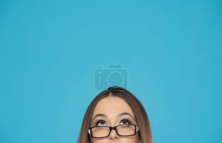 Photo for Half portrait of a young woman with glasses looking up on a blue background. - Royalty Free Image