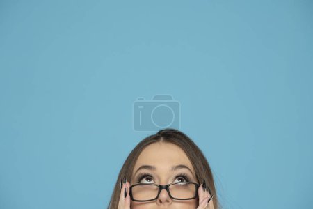 Téléchargez les photos : Demi portrait d'une jeune femme avec des lunettes levant les yeux sur un fond bleu. - en image libre de droit