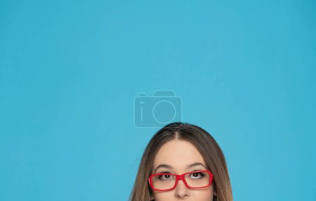 Foto de Medio retrato de una joven con gafas mirando hacia arriba sobre un fondo azul. - Imagen libre de derechos