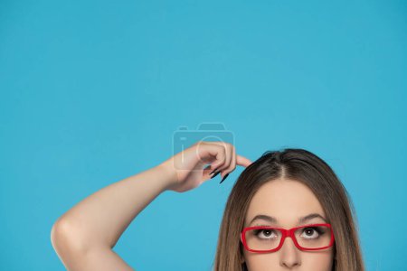 Foto de Medio retrato de una joven con gafas mirando hacia arriba y rascándole la cabeza. - Imagen libre de derechos