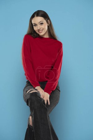 Foto de Linda chica sonriente en blusa roja y jeans negros aislados en el fondo del estudio azul - Imagen libre de derechos