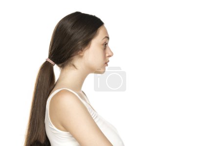 Téléchargez les photos : Vue du profil d'une belle jeune femme sans maquillage sur fond de studio blanc. - en image libre de droit
