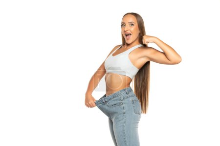 Photo for Successful weight loss, beautiful woman with too large jeans after effective diet on a white studio background - Royalty Free Image