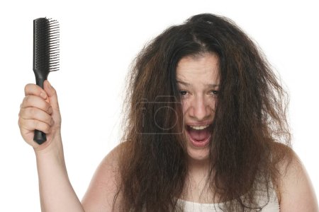 Téléchargez les photos : Portrait d'une jeune femme joufflue hurlante aux cheveux longs et salissants tenant une brosse à cheveux sur fond blanc. - en image libre de droit