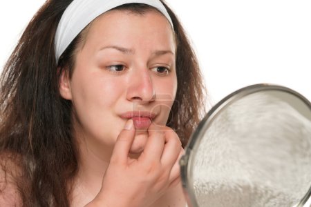 Téléchargez les photos : Jeune femme joufflue regarde sa bouche dans le miroir. Fond studio blanc - en image libre de droit