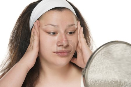 Téléchargez les photos : Jeune femme joufflue serrant sa peau de visage avec ses paumes sur un fond blanc. - en image libre de droit