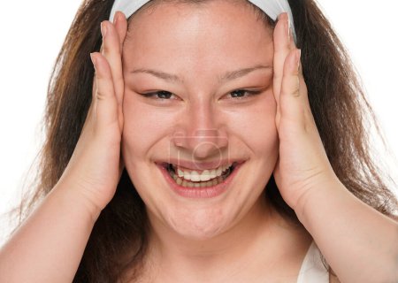 Téléchargez les photos : Jeune femme joufflue heureuse serrant la peau de son visage avec ses paumes sur un fond blanc. - en image libre de droit