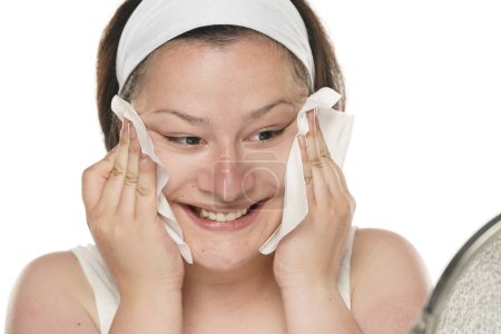 Foto de A young happy chubby woman removing makeup with the wet tissues  on white studio background. - Imagen libre de derechos