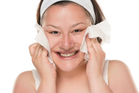 Foto de A young happy chubby woman removing makeup with the wet tissues  on white background. - Imagen libre de derechos