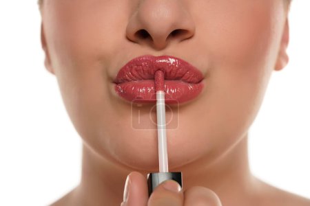 Téléchargez les photos : Image recadrée d'une jeune femme joufflue appliquant du brillant à lèvres sur un fond blanc. - en image libre de droit