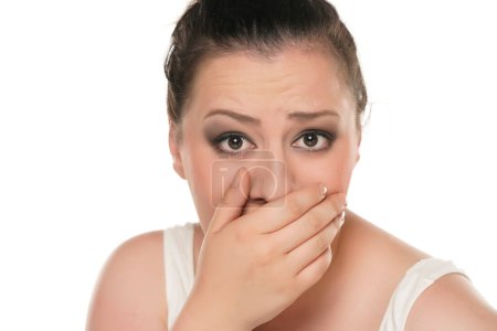 Photo for Chubby woman covering her mouth because bad breath on a white studio background - Royalty Free Image