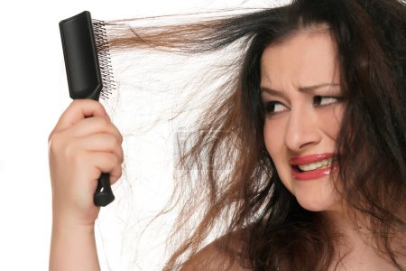 Téléchargez les photos : Portrait d'une jeune femme potelée nerveuse se brossant les cheveux longs sur fond de studio blanc. - en image libre de droit