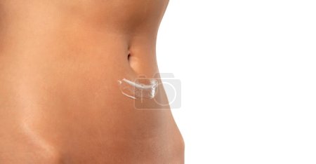 Téléchargez les photos : Close-up partial view of woman posing with body cream on belly on a white studio background - en image libre de droit