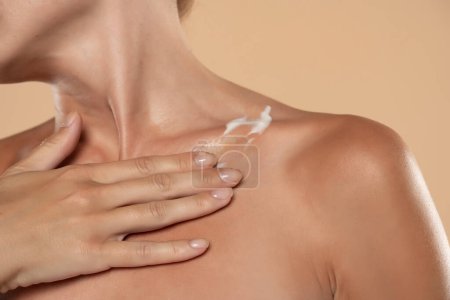 Téléchargez les photos : Woman apply body cream lotion on her chest on a beige studio background - en image libre de droit